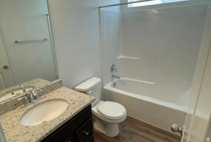 Full bathroom featuring a white tub/shower combination with a chrome fixture, a vanity with a granite-finish countertop and undermount sink, a large wall mirror, and wood-finish flooring