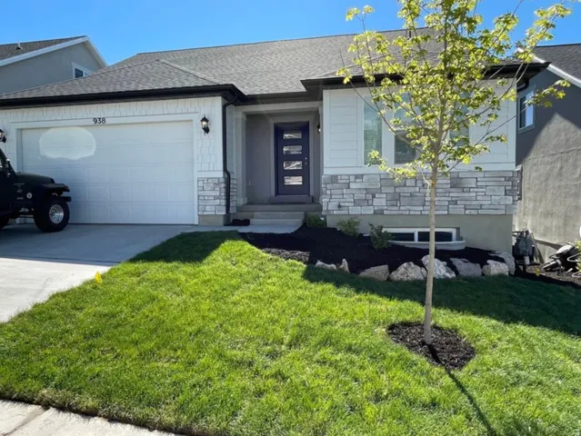 Modern facade featuring a two-car garage, stone and shingle siding, a dark entry door with frosted glass, and a landscaped front yard with a young tree