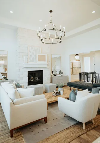 Spacious living area featuring a stone-clad fireplace with a classic mantel, a two-tiered chandelier, recessed lighting, and wood-finish flooring