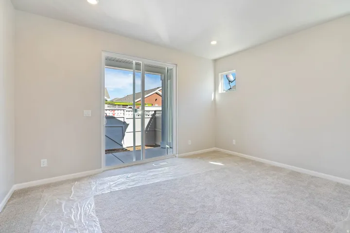 Light gray carpeted room with white walls, featuring a sliding glass door leading to an outdoor concrete patio