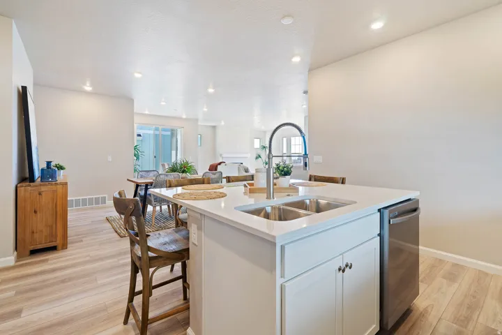 Contemporary kitchen island featuring a dual stainless steel sink with a high-arc faucet, integrated dishwasher, white cabinetry, and a light-toned countertop
