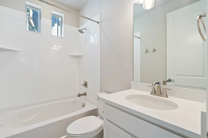 Bathroom featuring a white subway tile shower surround, brushed nickel fixtures, a white vanity with an undermount sink, and a large wall-mounted mirror