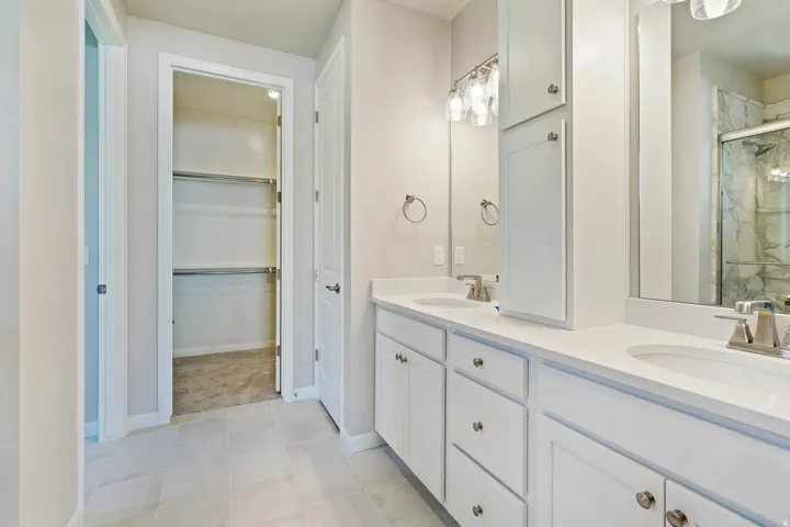 Bathroom featuring a double vanity with white cabinetry and integrated sinks, brushed nickel faucets, and a framed mirror