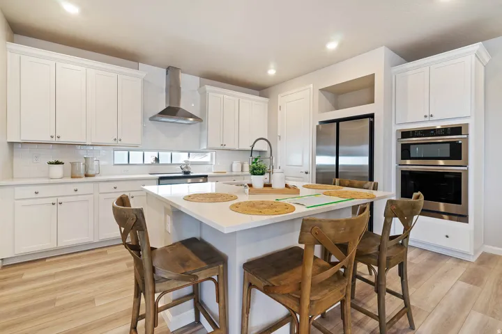 Contemporary kitchen featuring white shaker cabinetry, stainless steel appliances, a white subway tile backsplash, a large center island with a light-toned countertop, and wood-finish flooring