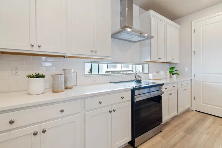 Bright kitchen featuring shaker-style white cabinetry, quartz countertops, a stainless steel range hood, a black electric range, and wood-finish flooring