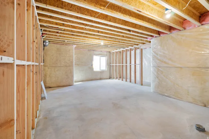 Unfinished basement featuring exposed wood framing, concrete flooring, and a visible window opening