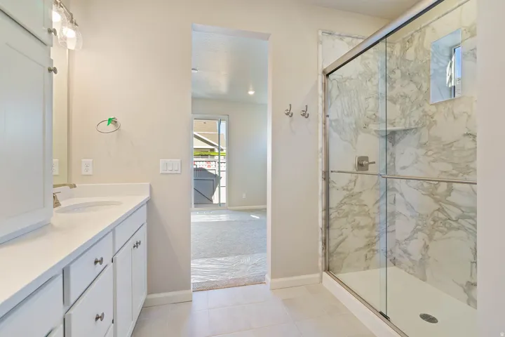 Spacious bathroom featuring a glass-enclosed shower with marbled wall tile, a white vanity with integrated sink, and brushed nickel fixtures