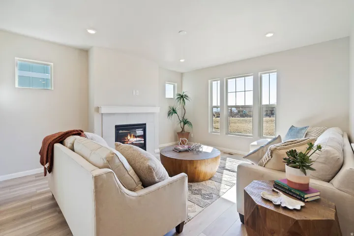 Living area featuring light wood-finish flooring, recessed lighting, a fireplace with a white mantel, and multiple large windows