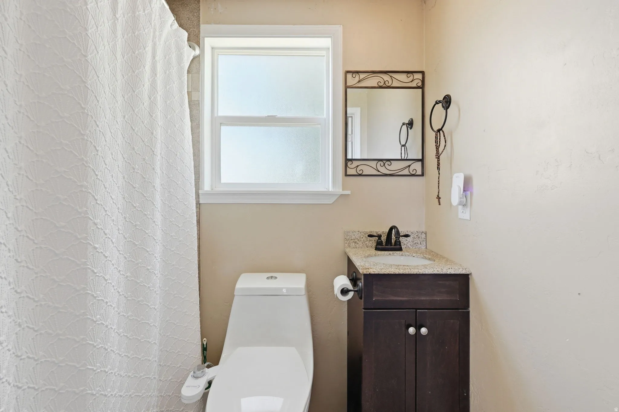 Bathroom featuring a single window, a compact vanity with a granite-style countertop, a dark wood-finish cabinet, and a decorative wall mirror