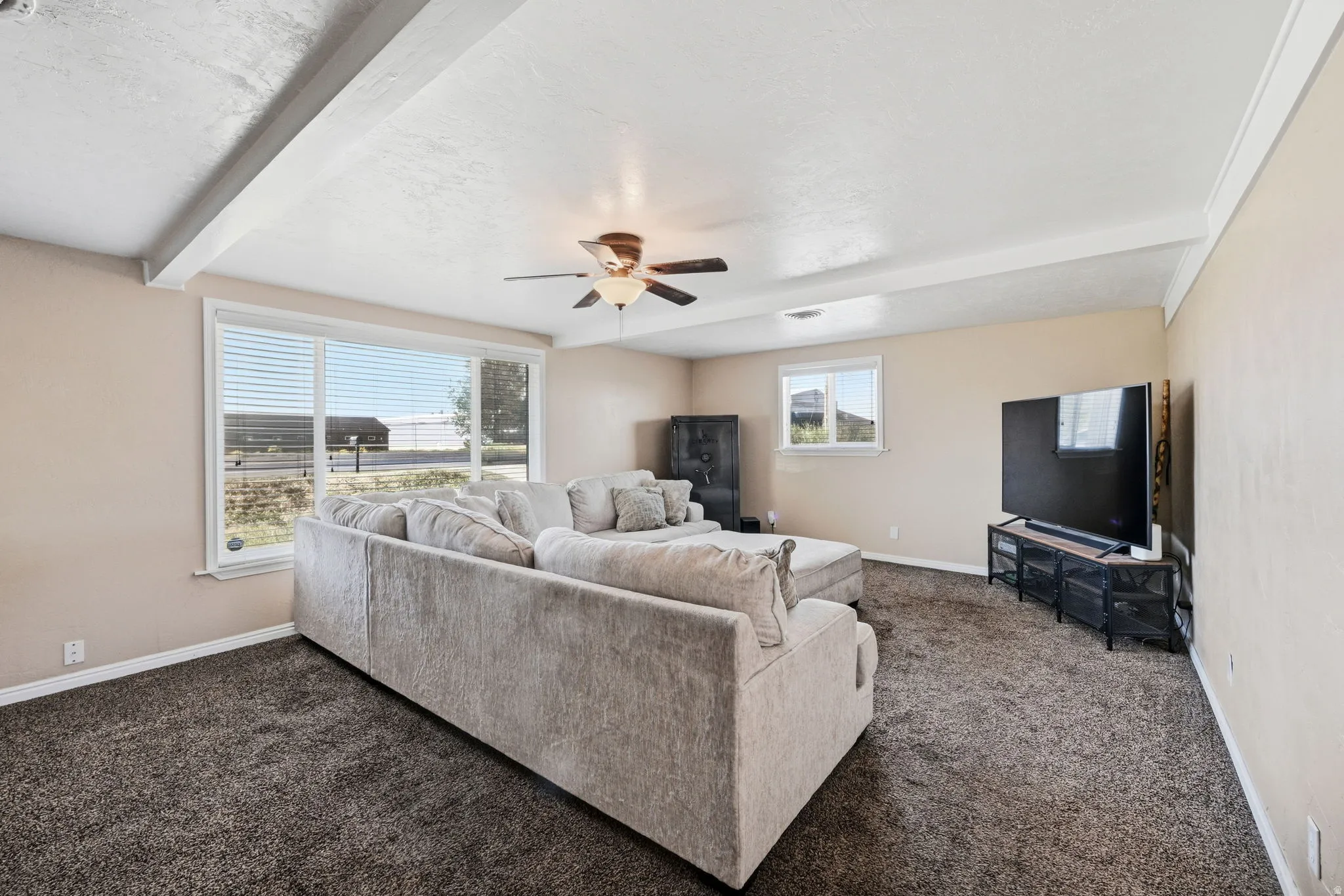 Spacious living area featuring textured carpet flooring, light-colored walls, and large windows with horizontal blinds