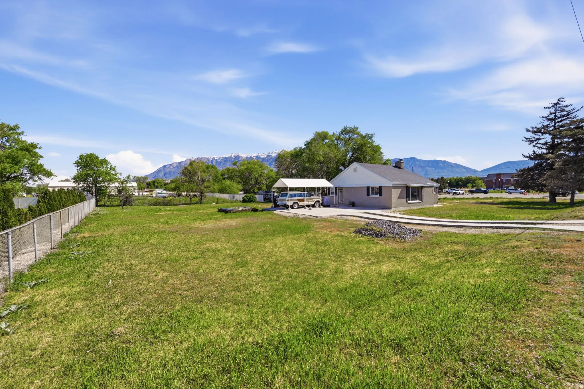 Expansive green space featuring a chain-link fence, mature trees, and a paved driveway