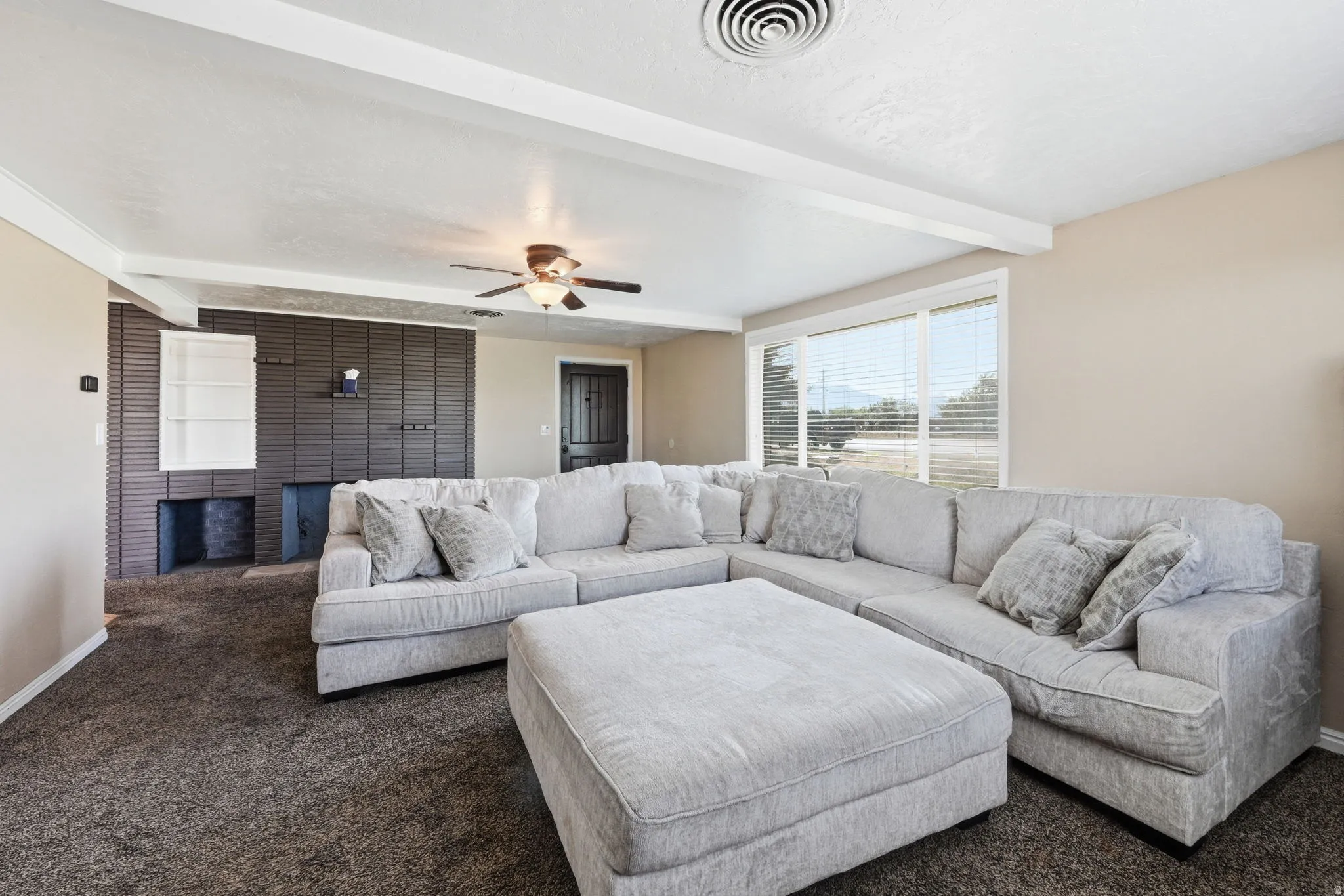 Spacious living area featuring a dark textured accent wall with built-in shelving, dark carpet flooring, and a ceiling fan