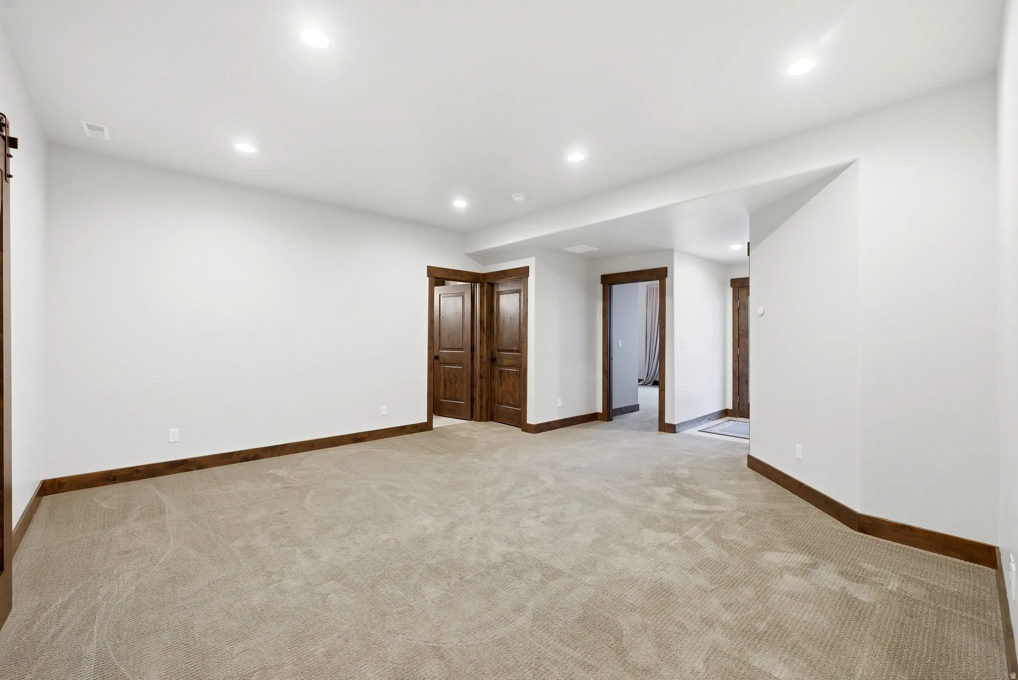Spacious carpeted room featuring recessed lighting, white walls, and dark wood-finish trim and doors