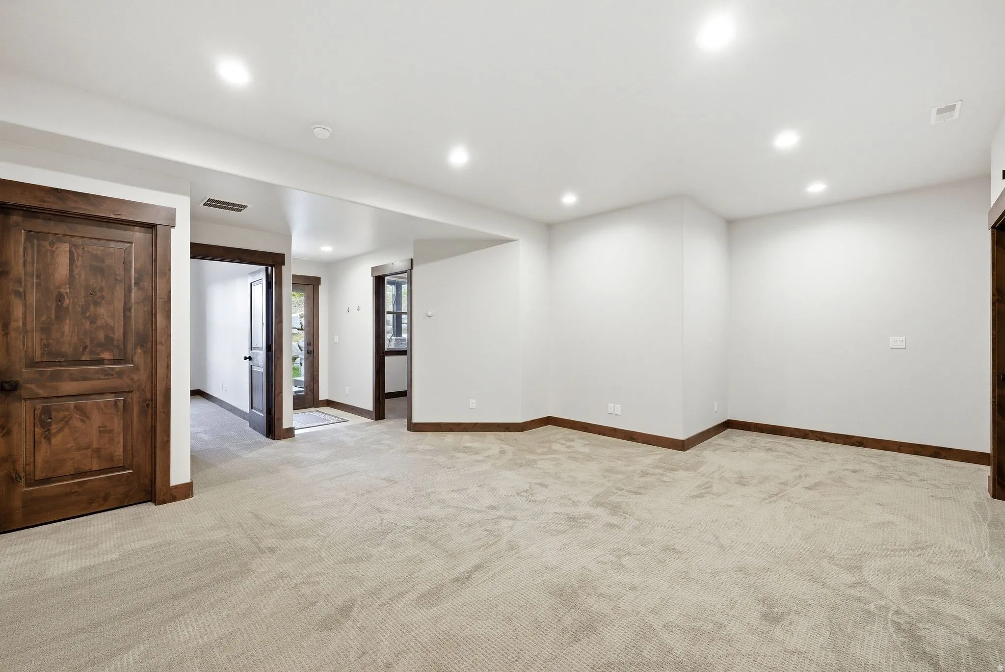 Spacious interior room featuring light-toned carpet flooring, recessed ceiling lighting, and crisp white walls