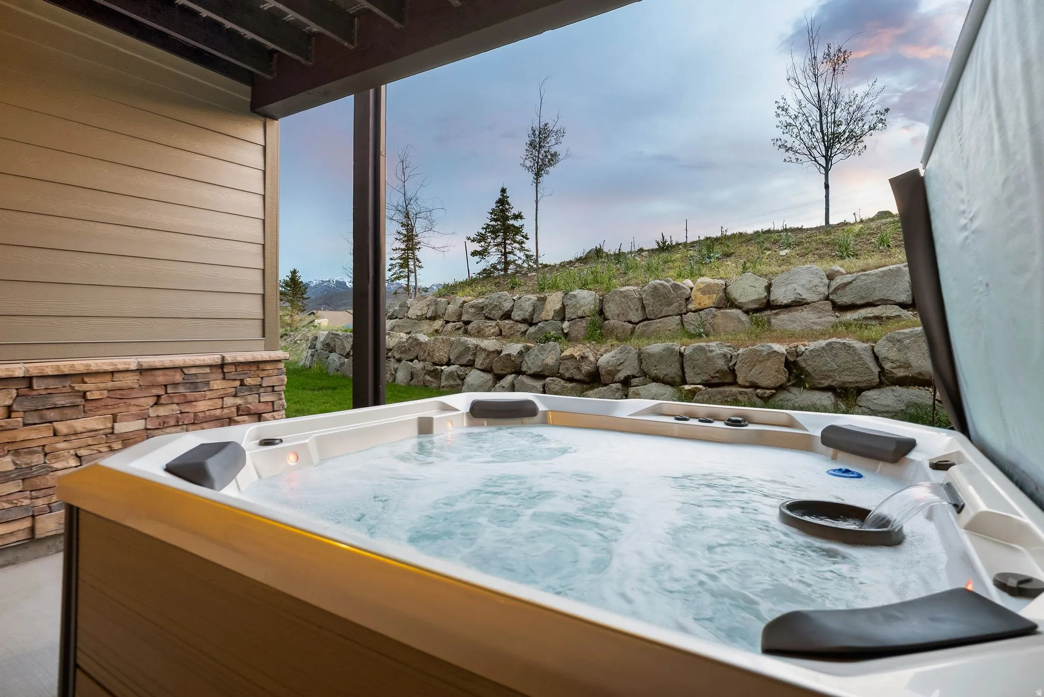 Bubbling outdoor spa on a concrete patio, featuring a stone retaining wall and a sloped grassy area