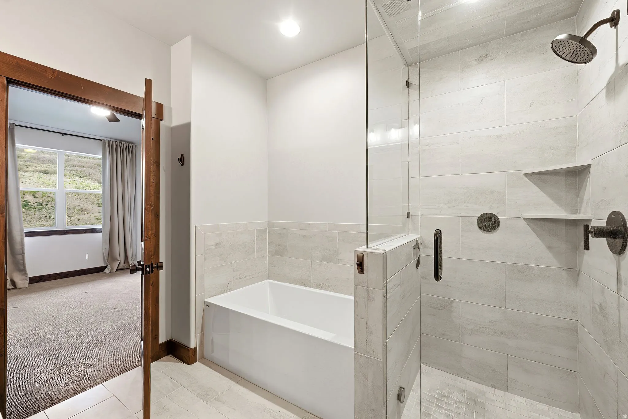 Contemporary bathroom featuring a deep soaking tub, glass-enclosed shower with tile surround, built-in shower shelving, and dark bronze fixtures