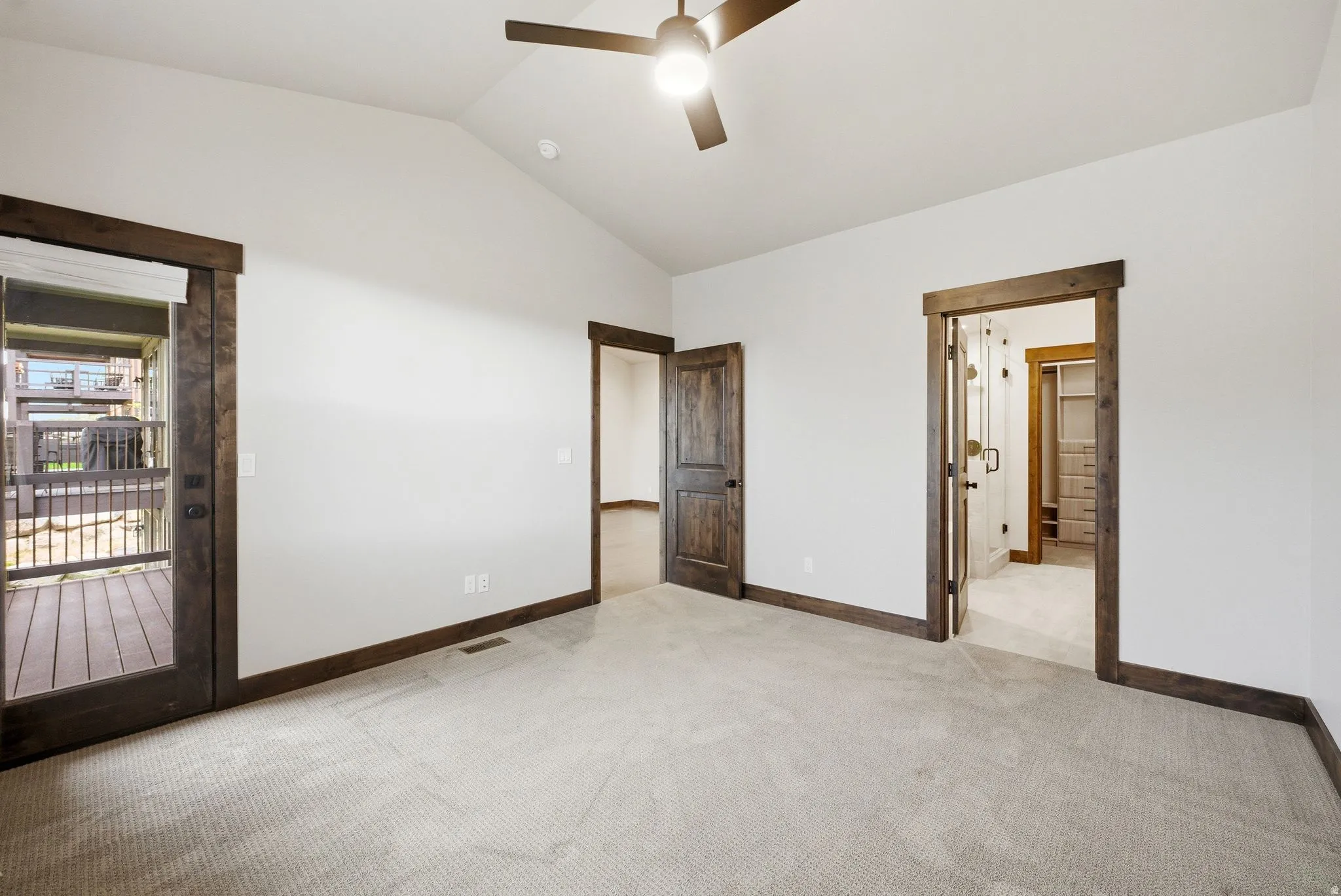 Vaulted ceiling room featuring carpet flooring, dark wood trim, a ceiling fan, and a glass-paneled door opening to an outdoor deck