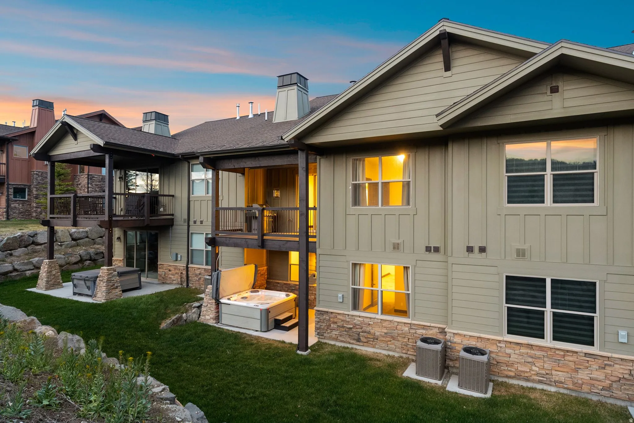 Multi-level exterior featuring balconies, a patio with a hot tub, and a rock retaining wall