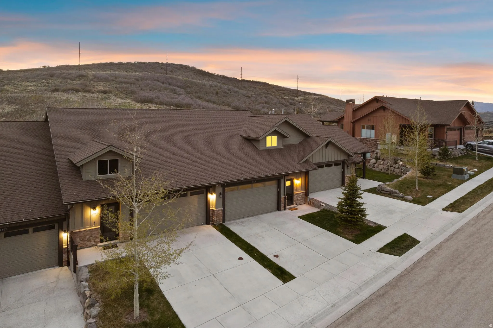 Townhome exterior featuring earth-toned siding, stone accents, multiple attached garages, concrete driveways, and mature landscaping