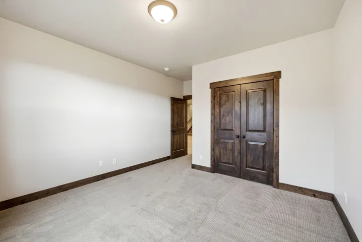 Spacious interior room featuring light gray carpet flooring, white painted walls, and dark wood-finish trim