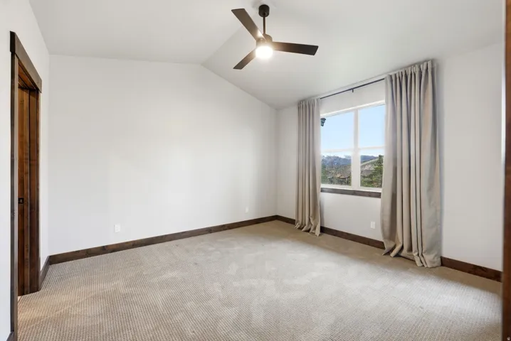 Spacious room featuring vaulted ceilings, a ceiling fan with integrated lighting, and neutral-toned carpeting