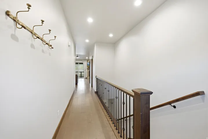 Hallway with wood-finish flooring, recessed ceiling lighting, and a dark wood staircase with wrought iron balusters