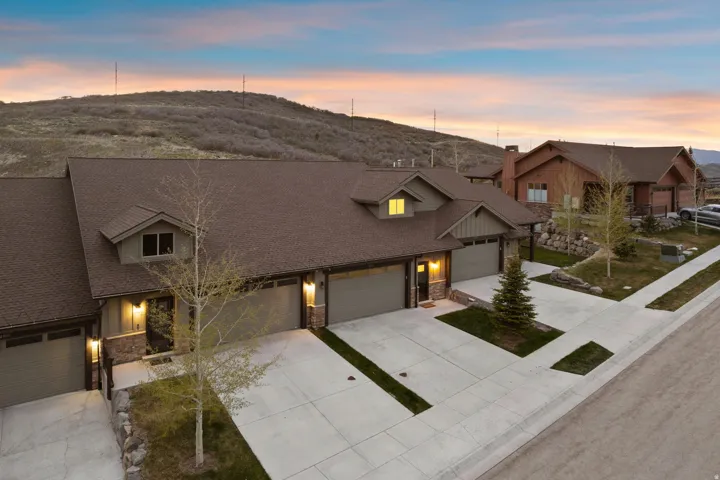 Townhome exterior featuring earth-toned siding, stone accents, multiple attached garages, concrete driveways, and mature landscaping