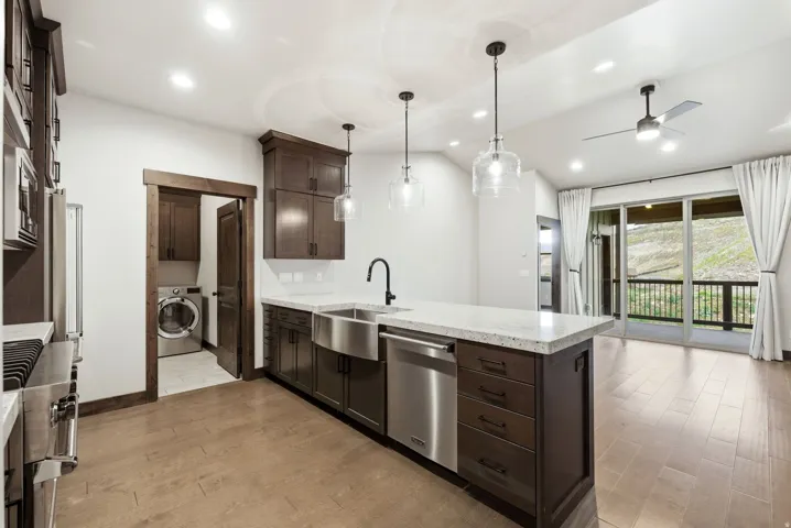 Open-concept kitchen with a large island featuring pendant lighting, integrated stainless steel appliances, and wood-finish flooring extending into the living area