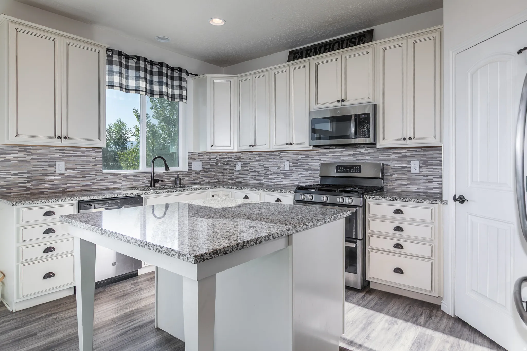 Kitchen featuring a central island with a granite-style countertop, white cabinetry with dark hardware, a tile backsplash, stainless steel appliances, and wood-finish flooring
