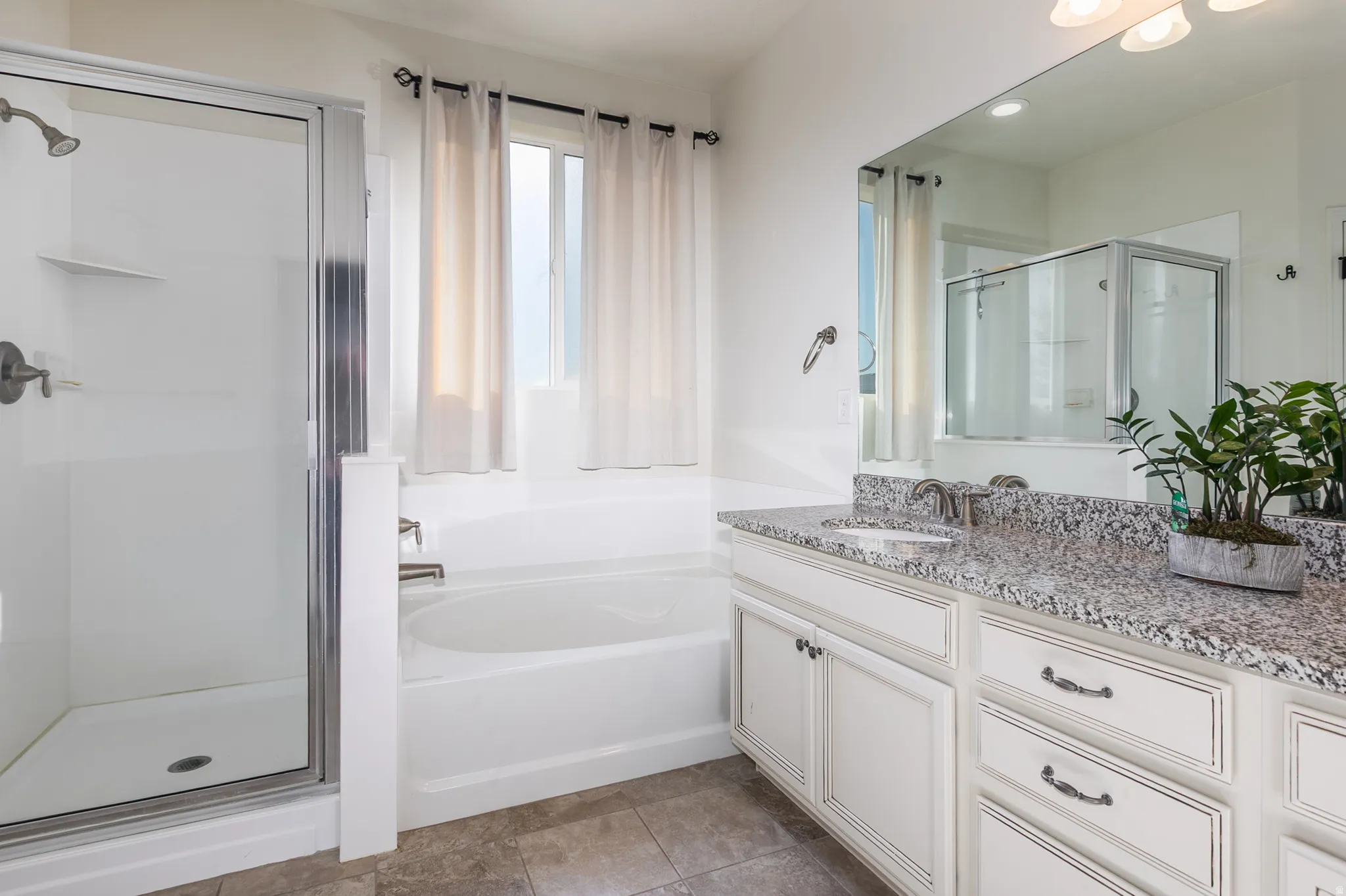 Bathroom featuring a separate shower enclosure with a glass door, a soaking tub, a double vanity with stone countertops, and white cabinetry