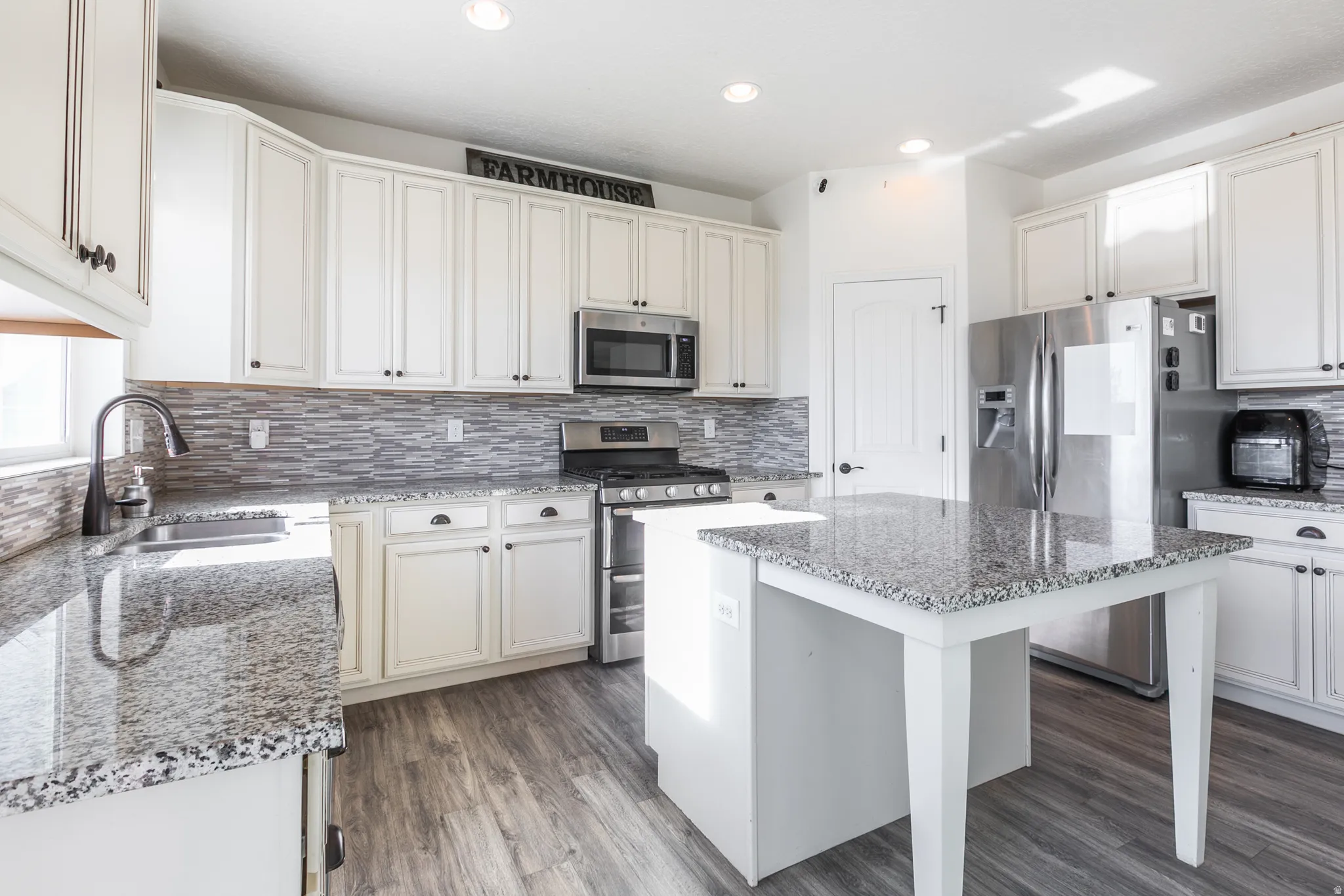 Kitchen featuring white shaker-style cabinetry, granite countertops, stainless steel appliances, a multi-tone tile backsplash, and wood-finish flooring