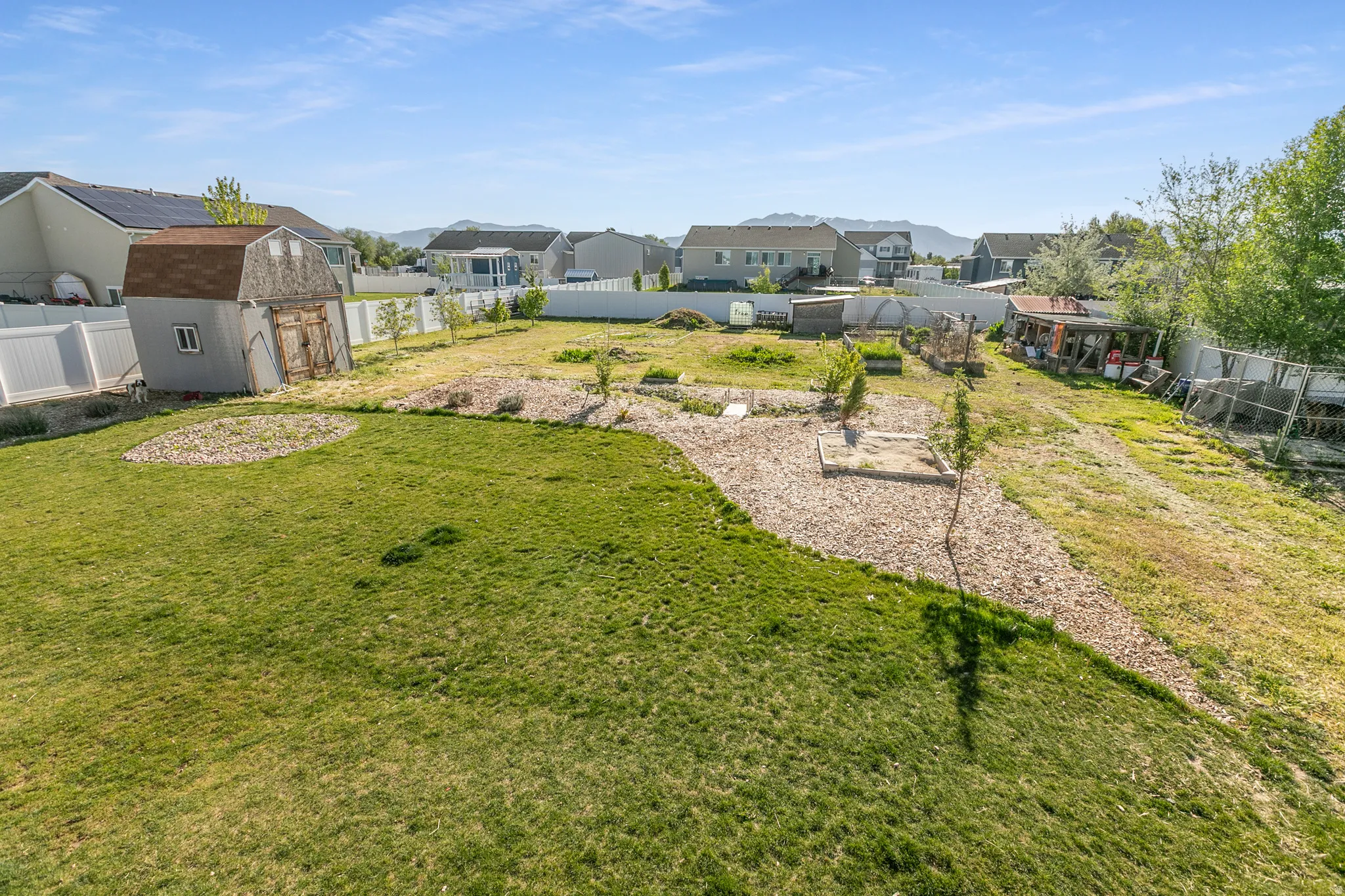 Expansive backyard featuring a combination of manicured lawn, gravel pathways, and cultivated garden beds