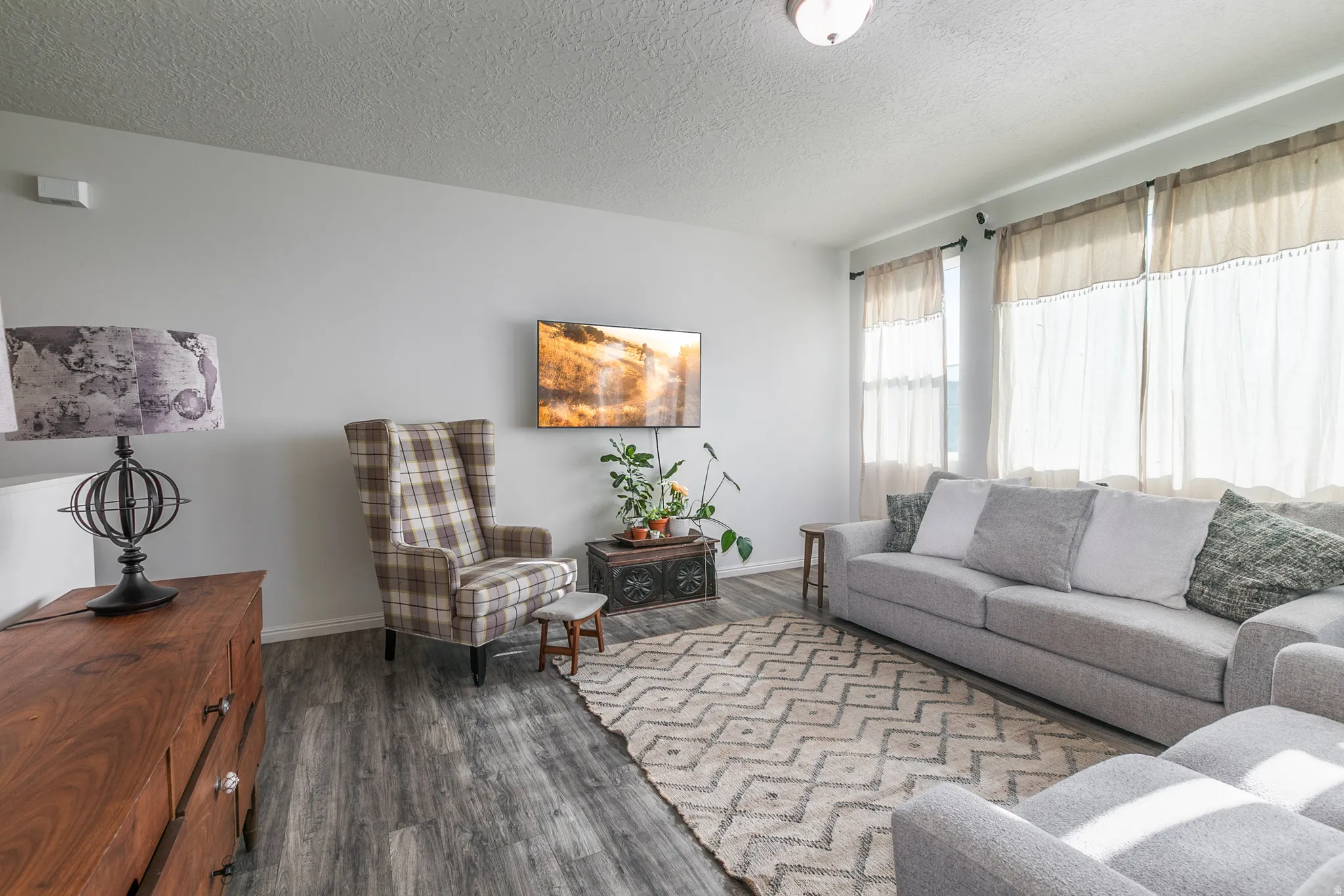 Spacious living area featuring wood-finish flooring, light gray walls, an overhead ceiling light, and multiple large windows