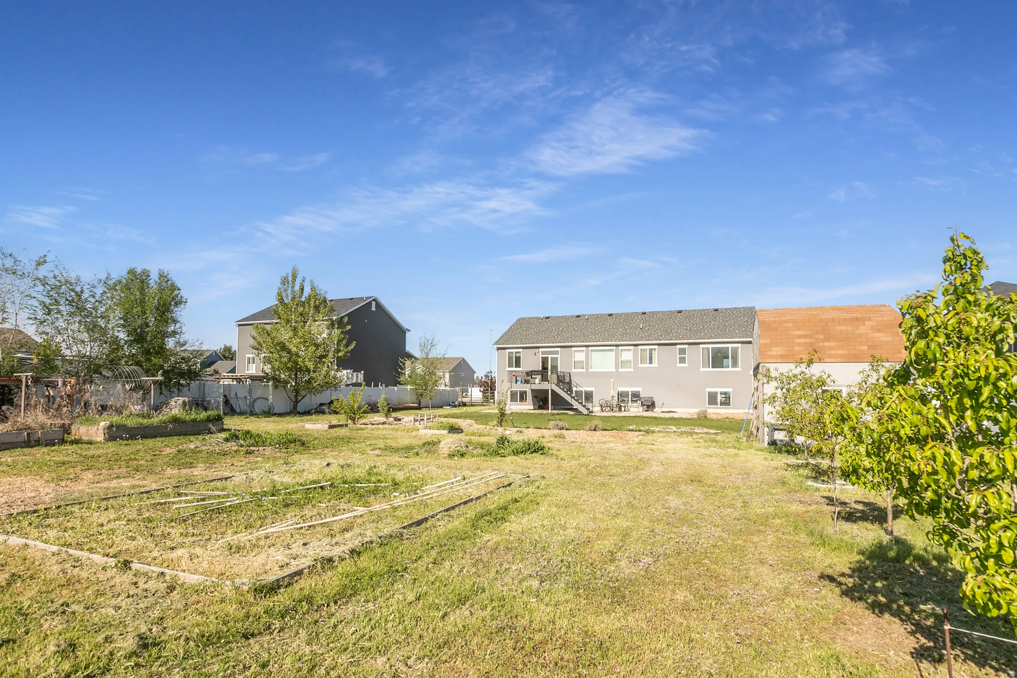 Expansive backyard featuring a partially fenced perimeter, mature trees, and defined garden beds