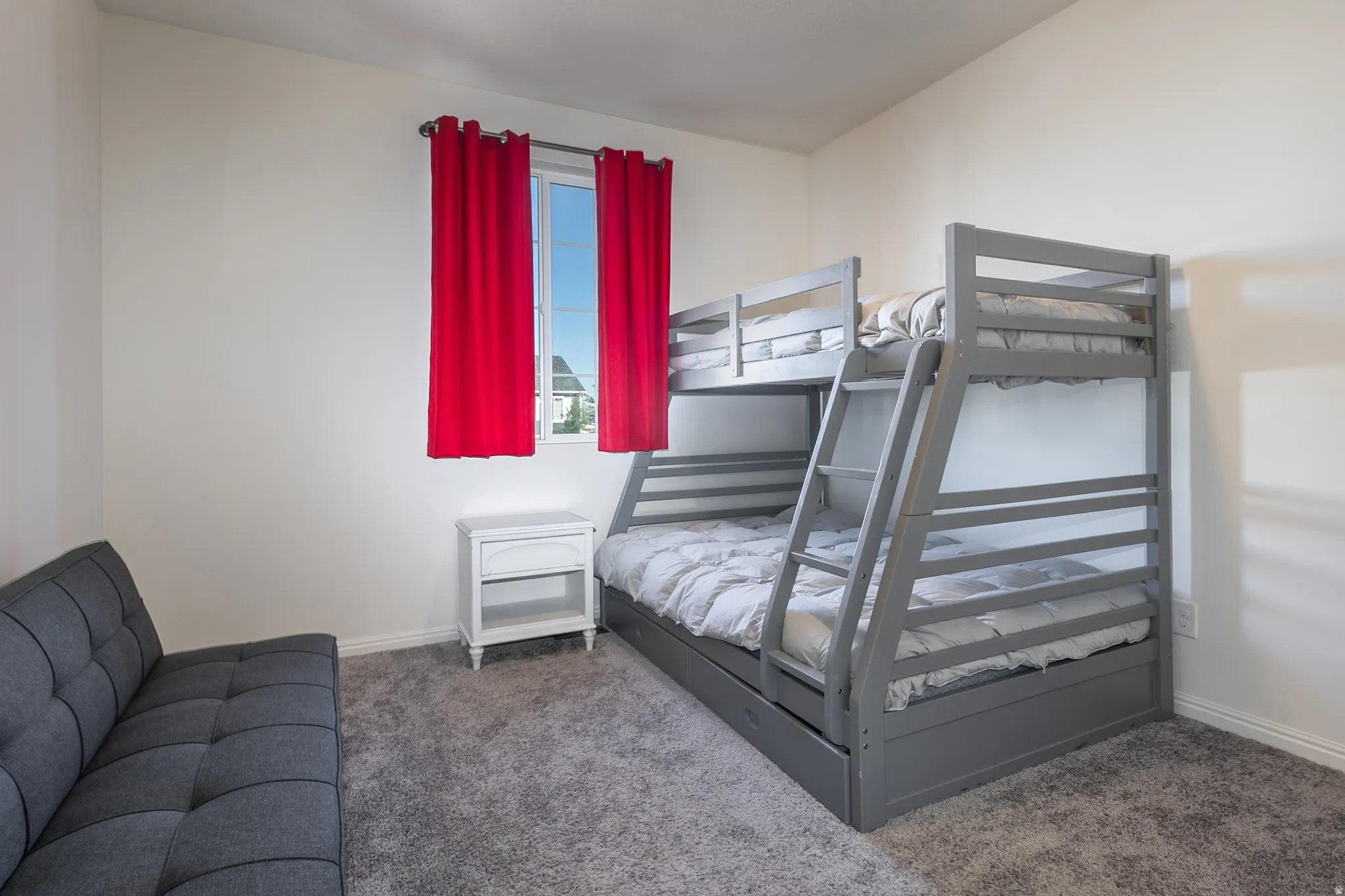 Bedroom featuring white walls, gray carpet flooring, and a window with red drapes