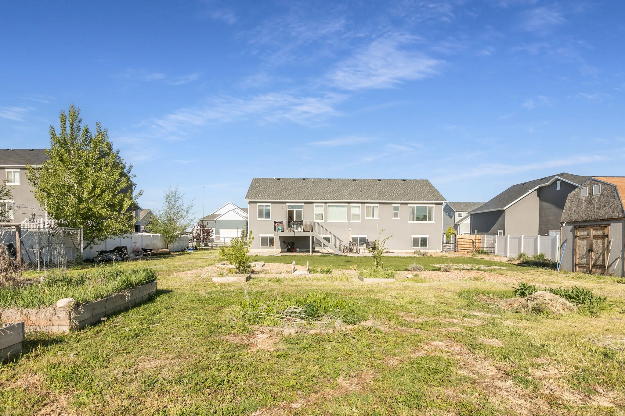Expansive backyard featuring a large green space, raised garden beds, a storage shed with a gambrel roof, a gray siding exterior, and a second-story deck