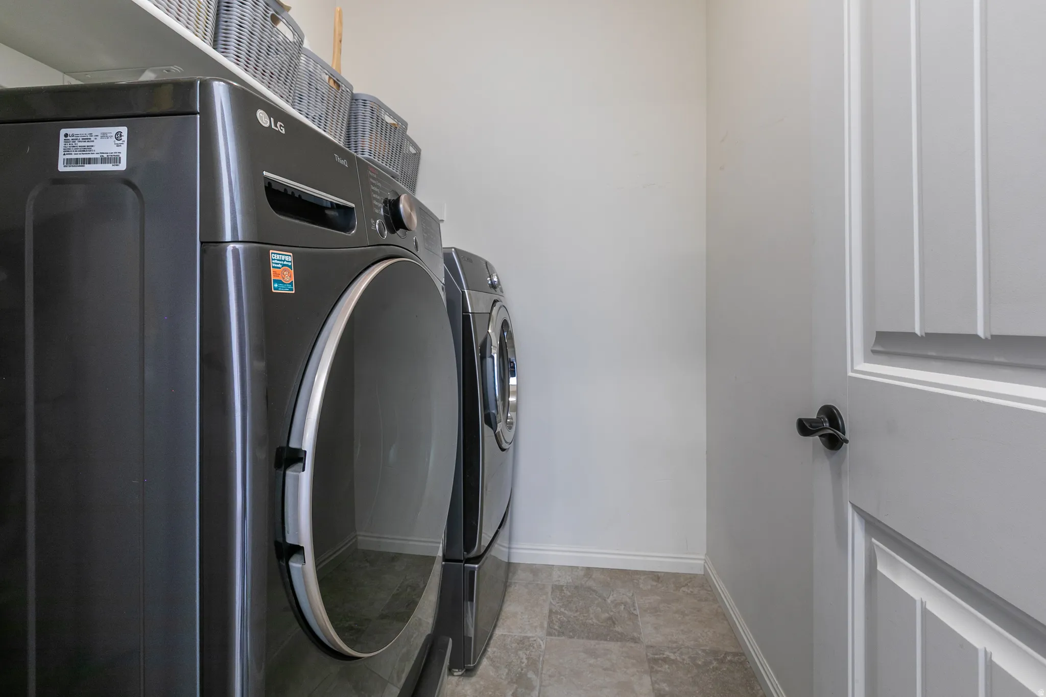 Laundry area with tile-finish flooring, white walls, and a white interior door with matte black hardware