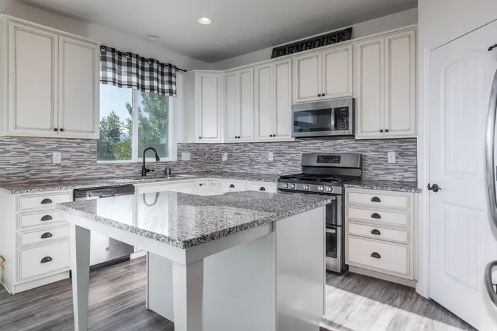 Kitchen featuring a central island with a granite-style countertop, white cabinetry with dark hardware, a tile backsplash, stainless steel appliances, and wood-finish flooring