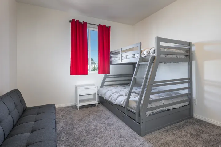 Bedroom featuring white walls, gray carpet flooring, and a window with red drapes