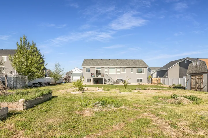 Expansive backyard featuring a large green space, raised garden beds, a storage shed with a gambrel roof, a gray siding exterior, and a second-story deck