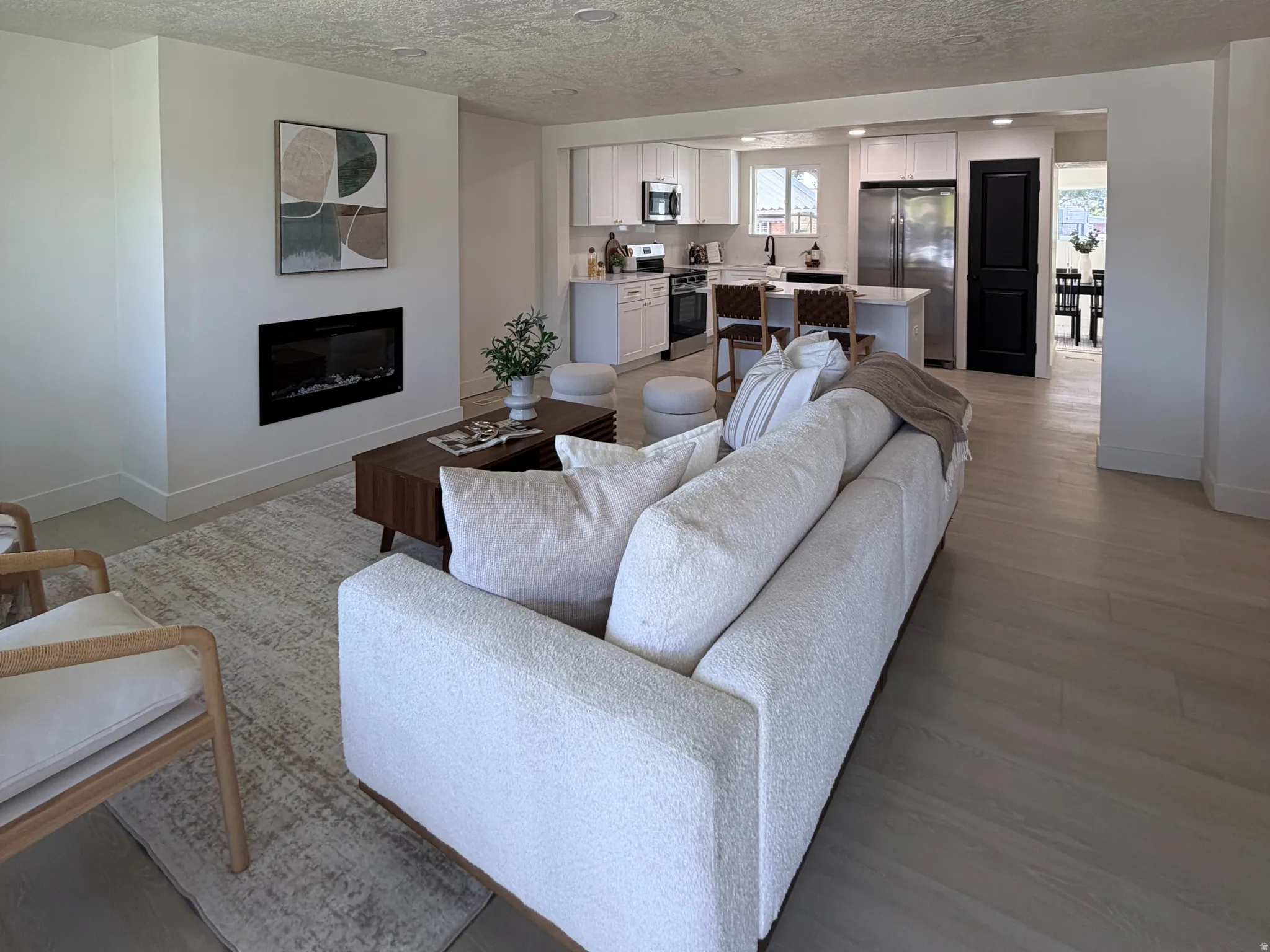Living area featuring light wood-type flooring, a glass covered fireplace, and a textured ceiling