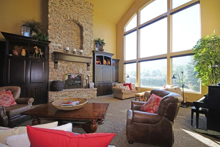 Expansive living area featuring a floor-to-ceiling stone fireplace, vaulted ceilings, and large picture windows