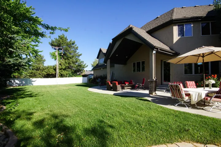 Spacious backyard featuring a manicured lawn, a large concrete patio, and mature trees
