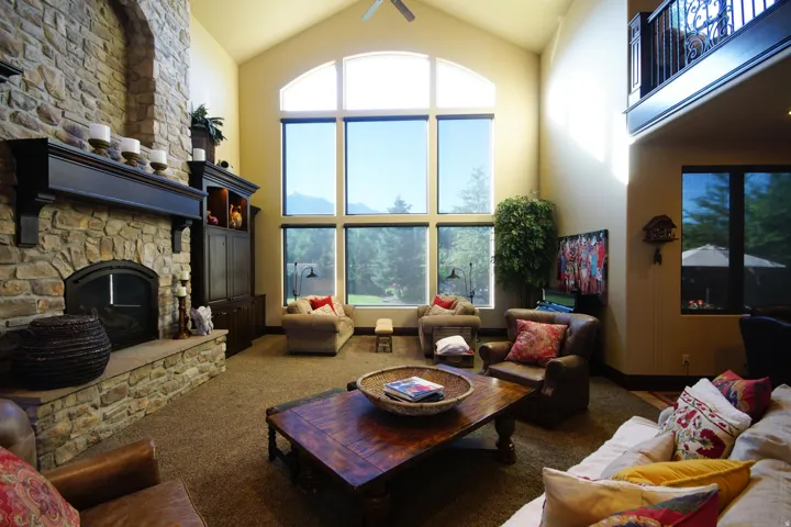 Great room featuring a floor-to-ceiling stone fireplace, vaulted ceiling, and an expansive window wall with an arched transom