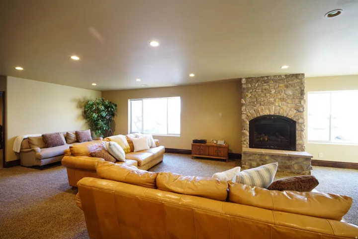 Spacious living area featuring a stone fireplace with arched firebox, two windows, recessed lighting, and carpeted flooring