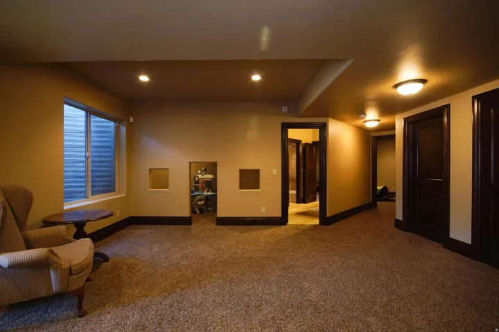 Carpeted room featuring a built-in recessed area, a window with horizontal blinds, and dark wood trim and doors