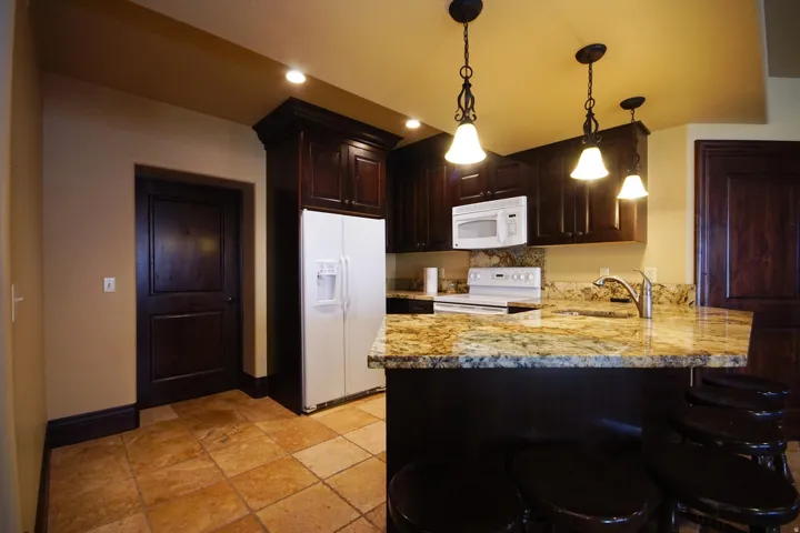 Kitchenette featuring dark wood cabinetry, granite countertops, white appliances, and a tiled floor