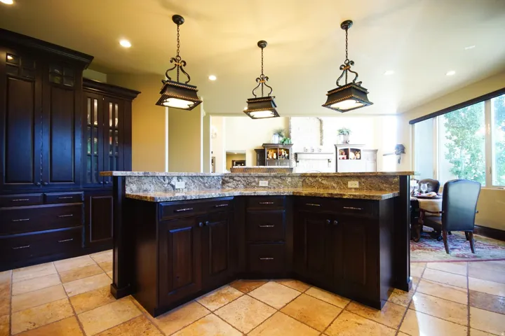 Kitchen island featuring dark wood cabinetry, a light-toned stone countertop, and three pendant light fixtures