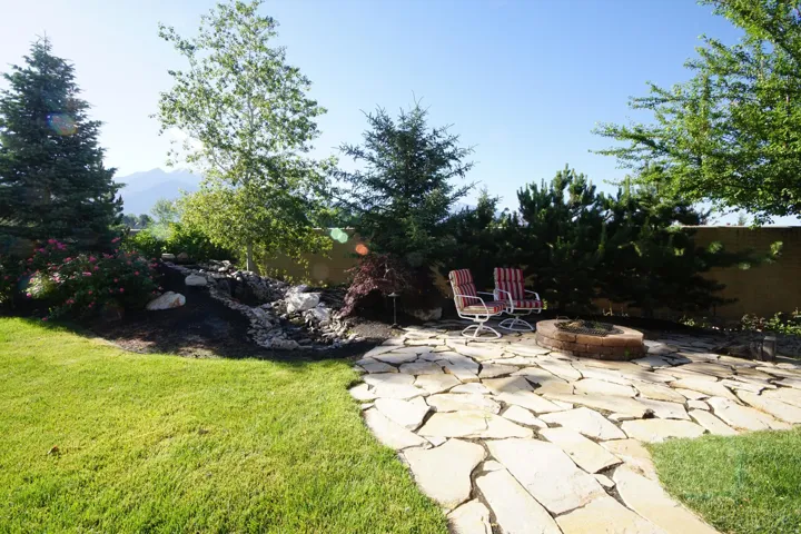 Expansive backyard featuring a natural stone patio, a built-in stone fire pit, and a rock-lined water feature