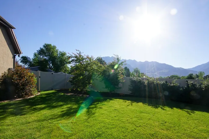 Expansive backyard featuring a manicured lawn, established shrubs, a privacy fence, mature trees, and a distant mountain backdrop